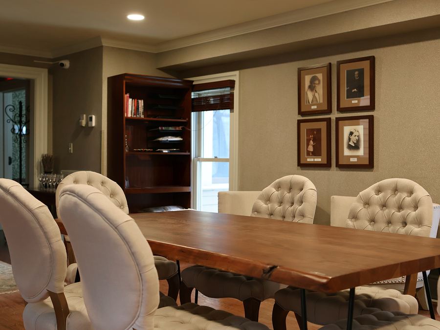 Dining room with a long wooden table, upholstered chairs and framed portraits on the wall